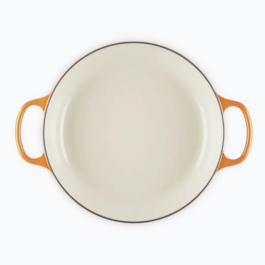 The shallow casserole with the lid off, showing the pale enamel interior and the wide flat base