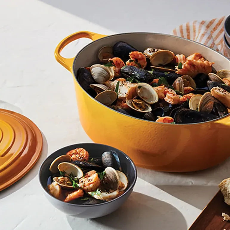The oval casserole full of mussels and clams on a laid table, lid resting beside it